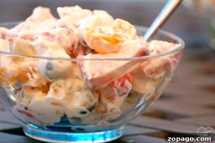 Easy fruit salad recipe that's super creamy and easy to make.. The perfect BBQ side dish or a light fruit dessert idea that everyone will love! A glass bowl of creamy fruit salad with Cool Whip and a spoon.