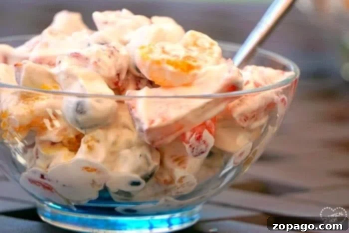 Easy fruit salad recipe that's super creamy and easy to make.. The perfect BBQ side dish or a light fruit dessert idea that everyone will love! A glass bowl of creamy fruit salad with Cool Whip and a spoon.