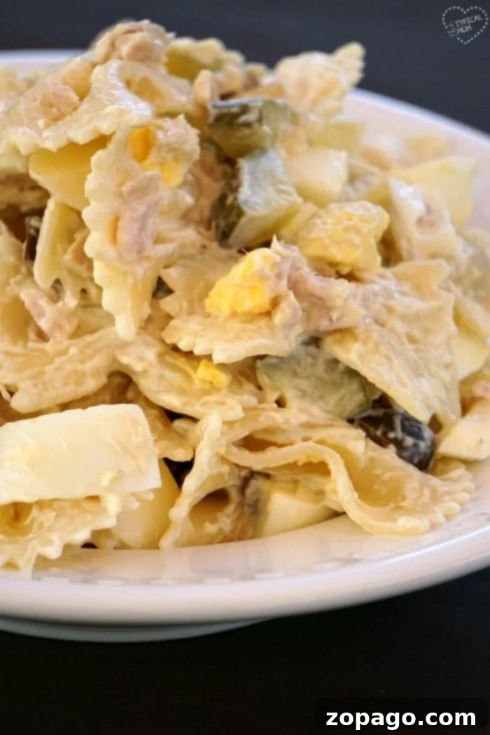 Enjoy a hearty serving of our loaded tuna macaroni salad. A close-up view of a serving of tuna pasta salad on a white plate, highlighting the creamy texture, colorful ingredients, and bowtie pasta.