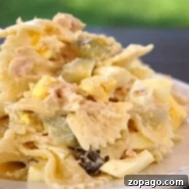 Creamy Tuna Macaroni Salad 2 A plate of tuna macaroni salad with bowtie pasta, diced pickles, and boiled egg sits against a blurred green background.