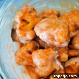 A glass bowl brimming with buffalo-baked cauliflower florets, each perfectly coated in vibrant orange buffalo sauce.