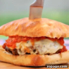Burgerizza 4 A New York pizza burger, featuring a patty topped with abundant melted cheese and vibrant tomato sauce, served on a toasted bun with a knife, all presented enticingly on a rustic wooden board.