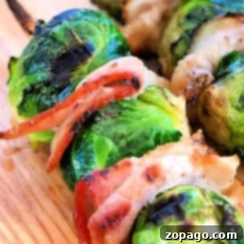 Grilled Brussels sprouts on skewers with bacon rest enticingly on a wooden board, garnished for serving.