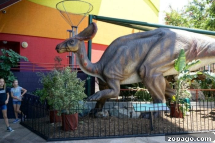 Outdoor dinosaur exhibit with a large walk-through dinosaur structure, featuring an animatronic dinosaur nearby at Discovery Cube OC