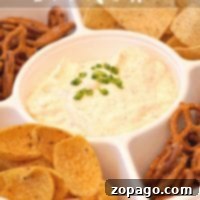 A divided tray showcasing the most incredible beer cheese dip recipe is adorned with chopped green onions and surrounded by a variety of pretzels, tortilla chips, and corn chips.