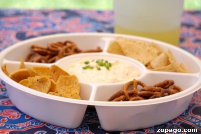 Pub-Style Beer Cheese Dip 3 A festive platter of cold beer cheese dip garnished with chives, surrounded by an array of crunchy pretzels and bread for dipping.