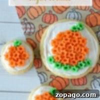 Three delightful pumpkin sugar cookies adorned with vibrant orange and green frosting rest on a charming pumpkin-patterned napkin.
