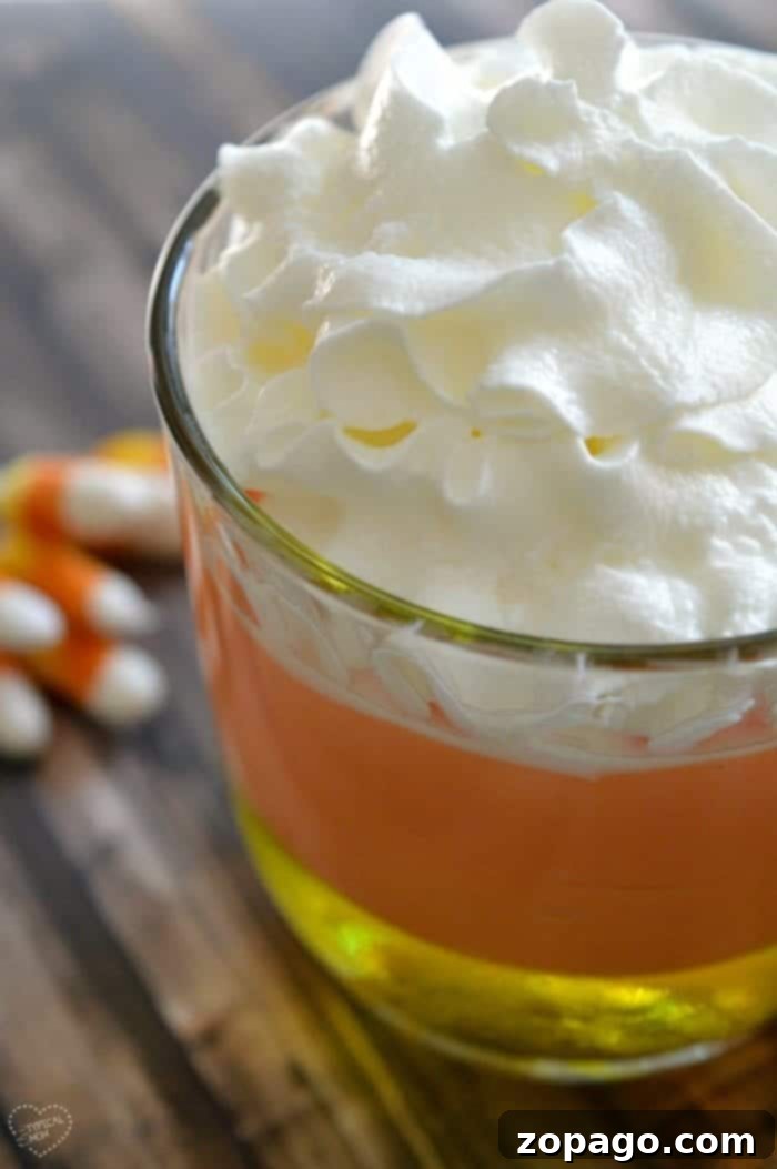 Halloween Candy Corn Jello Delight 2 A vibrant candy corn parfait with distinct yellow, orange, and white layers, garnished with whipped cream and candy corn, perfect for a festive Halloween treat.
