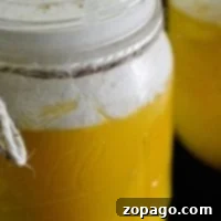 A glass jar brimming with creamy yellow pudding evokes the delightful flavor of an orange creamsicle drink, topped with a swirl of whipped cream and a delicate sprinkle of cinnamon.