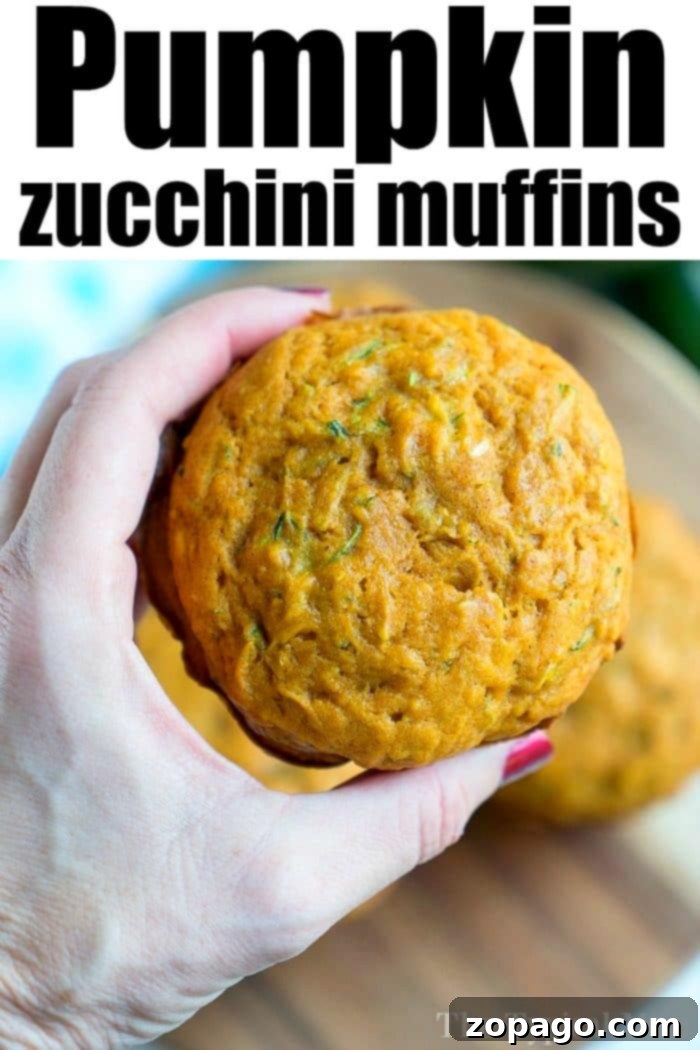 Homemade Pumpkin Zucchini Muffins A hand presents a perfectly baked pumpkin zucchini muffin against a rustic wooden board, highlighting its deliciousness.