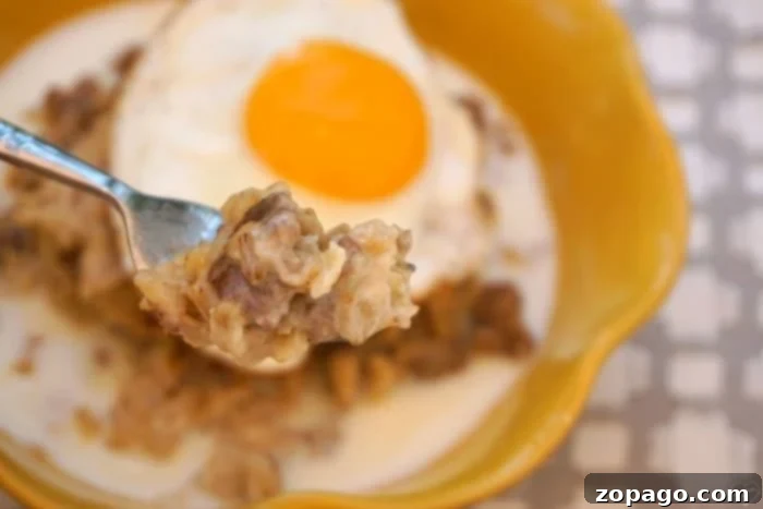A hearty serving of savory oatmeal with sausage, egg, and green garnish.