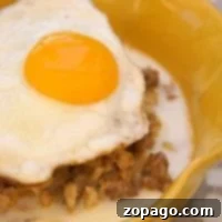 A delicious take on breakfast, this sausage and egg savory oatmeal is topped with a perfectly fried egg with a runny yolk, all served in a vibrant yellow bowl.