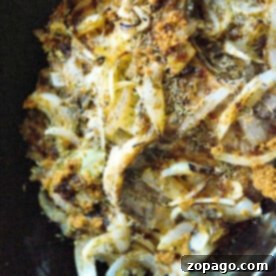 Tender Crockpot Pork Chops 3 Close-up of a dish featuring seasoned onions and herbs on crockpot pork chops in a slow cooker.