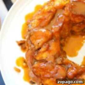 Close-up of a glazed pumpkin monkey bread ring on a white plate, with a caramel-like drizzle on top. Made using cinnamon rolls, it offers layers of spicy sweetness perfect for autumn indulgence.
