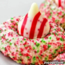 A close-up of a Hershey Kiss Christmas cookie topped with a striped chocolate, coated in red and green sugar sprinkles for a festive touch, on a baking sheet.