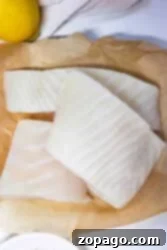 Crispy Oven-Baked Fish 4 Three raw fish fillets on parchment paper, ready for cutting and breading