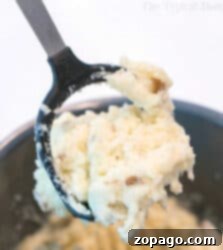 Creamy Slow Cooker Mashed Potatoes 6 A potato masher in a slow cooker, mixing creamy mashed potatoes.