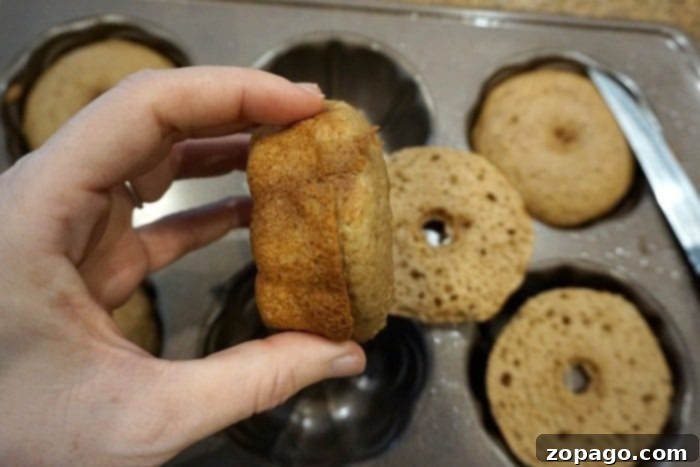 Simple Pumpkin Bundt Bites 4 A hand gently holds a small pumpkin cake crafted from cake mix over a tray adorned with mini Bundt cakes.