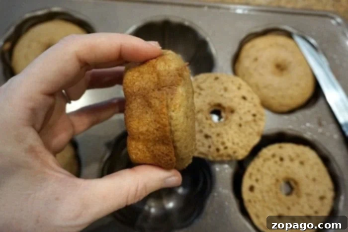 Easy Pumpkin Bundtlets 4 A hand gently holds a small pumpkin cake crafted from cake mix over a tray adorned with mini Bundt cakes.