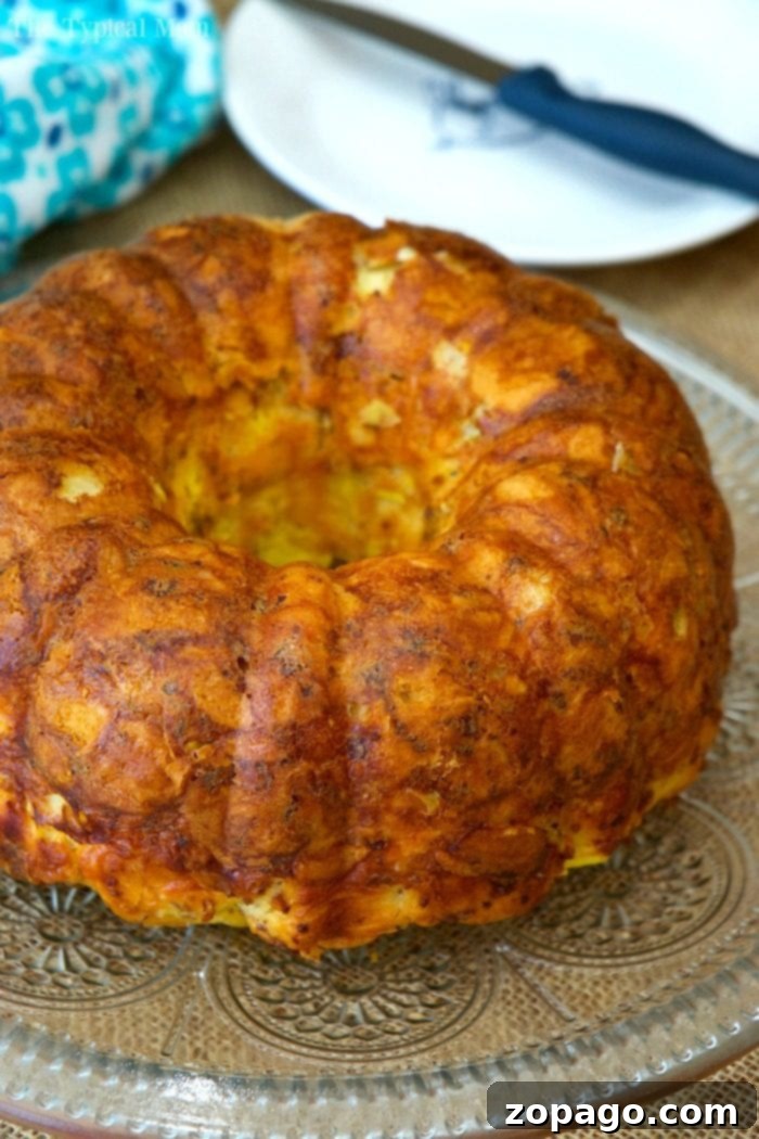 Delicious and easy Bacon, Egg, and Cheese Breakfast Bundt Cake with Biscuits for a perfect brunch or holiday meal. Golden brown Bacon, Egg, and Cheese Breakfast Bundt Cake on a platter, ready to be sliced, highlighting the fluffy biscuit texture.