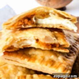A close-up of flaky hand pies with creamy, orange pumpkin filling, stacked on a wooden surface, showcases the enticing aroma of these air fryer creations.