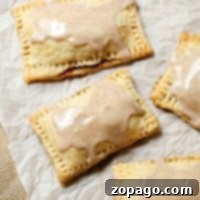 Four homemade pop tarts with icing sit invitingly on parchment paper, promising a delightful treat.