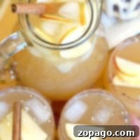 A pitcher and glasses brimming with chilled sparkling apple cider, ice, apple slices, and cinnamon sticks grace the table.