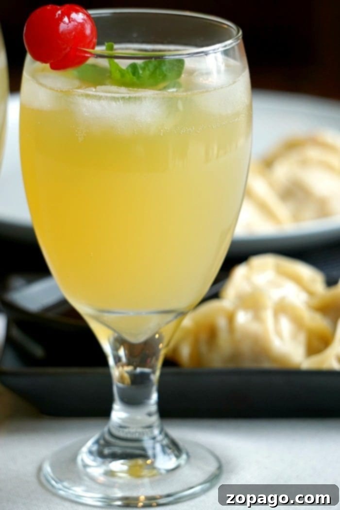 Sparkling Island cocktail is what to call this favorite pineapple drink of mine! Goes perfectly with any meal really and easy to create with rum and pineapple juice. Cocktail or mocktail directions. #pineapple #cocktail #drink #mocktail #punch A glass of sparkling Malibu Bay Breeze, elegantly garnished with a cherry and mint, sits enticingly in the foreground, while savory dumplings temptingly linger in the blurred background, creating a perfect pairing scene.