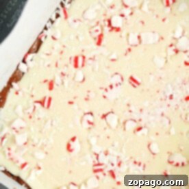 Microwave peppermint fudge with a layer of white chocolate and crushed peppermint topping, all set atop a decadent sheet of chocolate fudge in a baking pan.