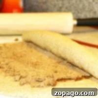 Cozy Gingerbread Cinnamon Rolls 3 A delicious dough is being skillfully rolled with cinnamon and sugar, hinting at the creation of irresistible gingerbread cinnamon rolls, with a trusty rolling pin in the background.