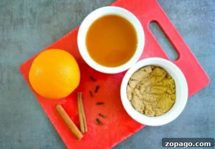 Crockpot hot apple cider is amazing, especially during the holidays! This one is so easy to make and stays warm for hours in the slow cooker! #crockpot #slowcooker #apple #cider #hot #drinks A red cutting board holds an orange, a small bowl of brown sugar, a small bowl of liquid, cinnamon sticks, and cloves on a gray surface—perfect ingredients for crafting crockpot hot apple cider.