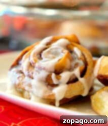 A close-up of Bisquick Cinnamon Rolls topped with icing on a white plate.