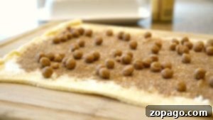 Rolled-out crescent roll dough topped with cinnamon, sugar, and pecans on a wooden board.