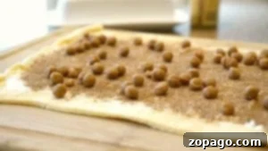 Rolled-out crescent roll dough topped with cinnamon, sugar, and pecans on a wooden board.
