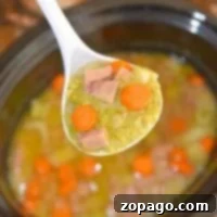 Easy Slow Cooker Split Pea Soup 2 A ladle of slow cooker split pea soup with ham and carrots over a crockpot.