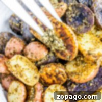 A plate of roasted potato medley, vibrant in tricolor hues and generously coated in pesto, with a fork lifting one perfect slice.