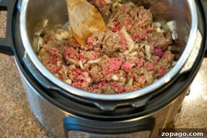 Instant Pot lasagna soup is amazing and healthy!! You can make it in the slow cooker too but in your pressure cooker it's done in just 8 minutes! #lasagnasoup #lasagna #soup #instantpot #pressurecooker #instantpotrecipes #thetypicalmom Ground beef and chopped onions are being cooked to perfection in an Instant Pot, preparing the base for a flavorful lasagna soup.