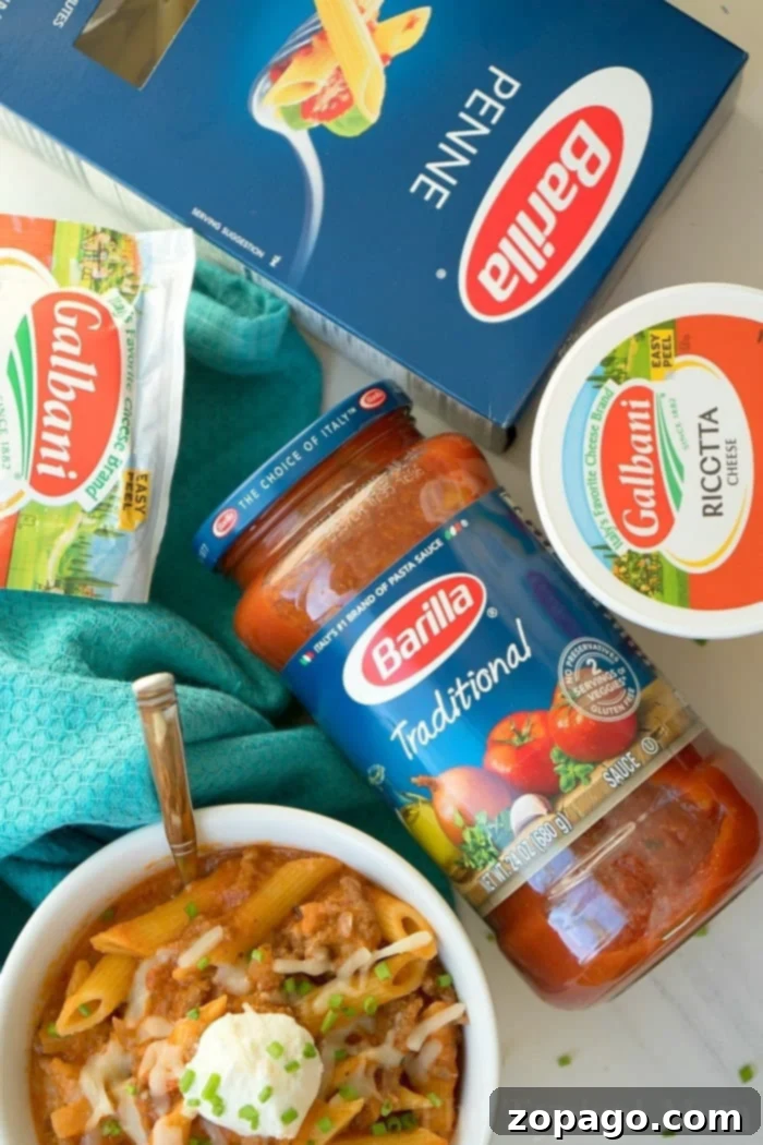 Effortless Instant Pot Lasagna Soup 4 A colorful flat-lay showcasing ingredients for a pasta dish: a box of Barilla penne, a jar of Barilla Traditional pasta sauce, a container of Galbani ricotta cheese, and a package of Galbani mozzarella cheese. A prepared bowl of instant pot lasagna soup is also included.