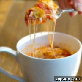 Speedy Biscuit Mug Pizza 2 A hand lifts a spoonful of cheesy pizza in a mug.
