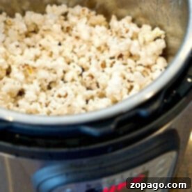 A metal pot brimming with freshly popped popcorn sits in an Instant Pot on the countertop. The control panel of the cooker is visible, showcasing a digital display.