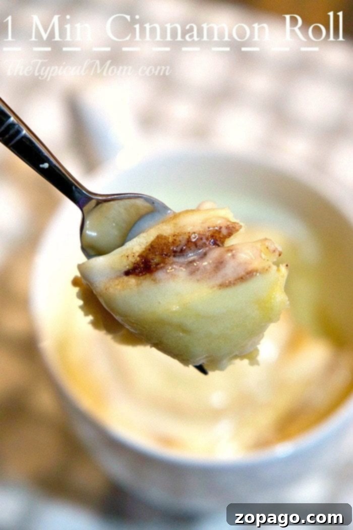 Mug Cinnamon Roll 2 Close-up of a spoon lifting a piece of warm, frosted cinnamon roll from a mug, highlighting the gooey texture.