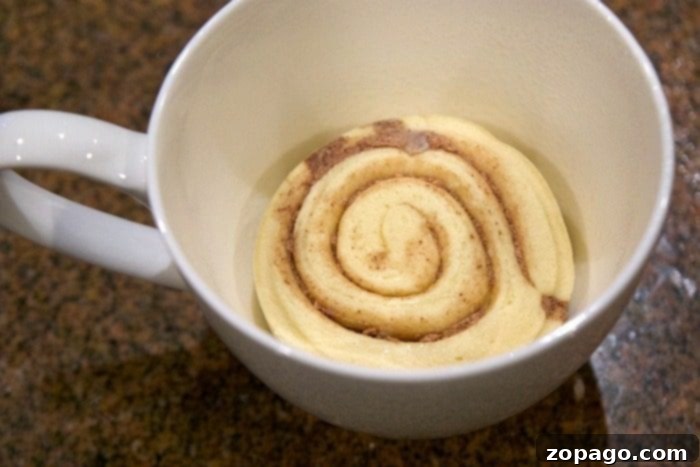 Mug Cinnamon Roll 3 A close-up shot of a warm cinnamon roll in a white mug, topped with smooth white frosting.
