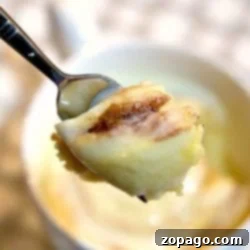 Close-up of a spoon holding a piece of cinnamon roll above a mug, ready for eating.