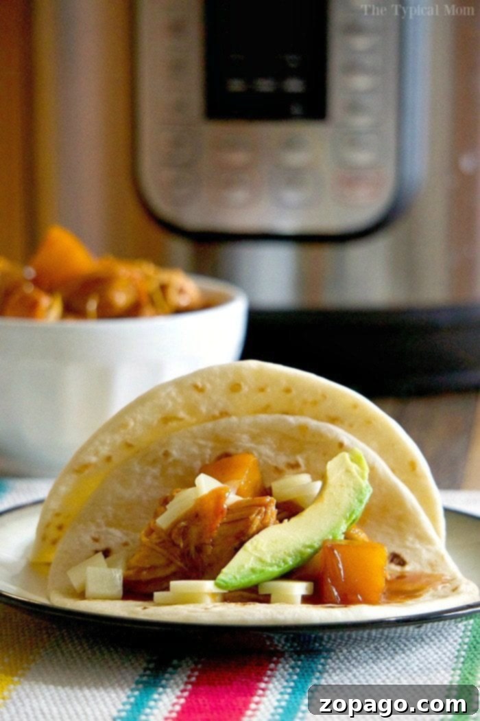 A close-up of tender, barbecue-smothered shredded chicken in a Ninja Foodi pressure cooker, with tongs lifting a portion.