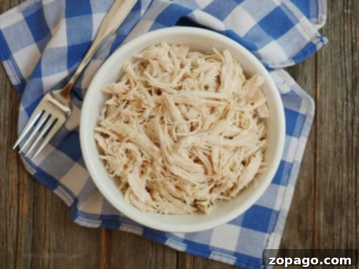Close-up of shredded chicken simmering in sauce within an Instant Pot, with steam rising.