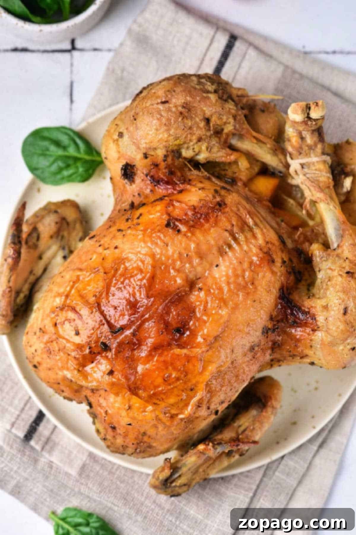 Best Instant Pot whole chicken recipe ever! If you're looking to cook an entire chicken in your pressure cooker it's never been easier using these instructions. Placed on edible trivets the whole thing is cooked and ready to eat in just 25 minutes flat. You'll never use your oven again. #instantpotrecipes #pressurecooker #wholechicken #moist #easy #instructions #crockpotexpress #thetypicalmom Instant Pot whole chicken with crispy golden skin served on a white plate, garnished with fresh spinach leaves.