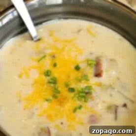 A bowl of creamy Instant Pot potato cheese soup, topped with shredded cheese and chopped herbs, with a spoon.
