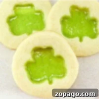 Learn how to make stained glass cookies with three delightful treats featuring green shamrock-shaped translucent centers, elegantly displayed on a light surface.