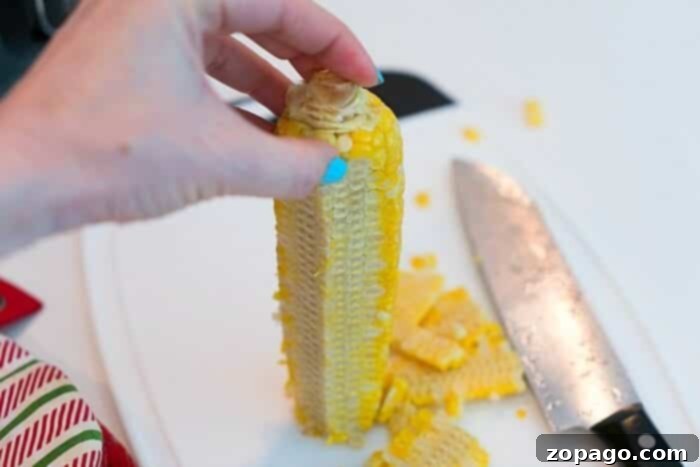 Creamy Instant Pot Potato Corn Chowder 2 Close-up shot demonstrating how to safely and efficiently cut fresh corn kernels off the cob, a key step for homemade corn chowder.