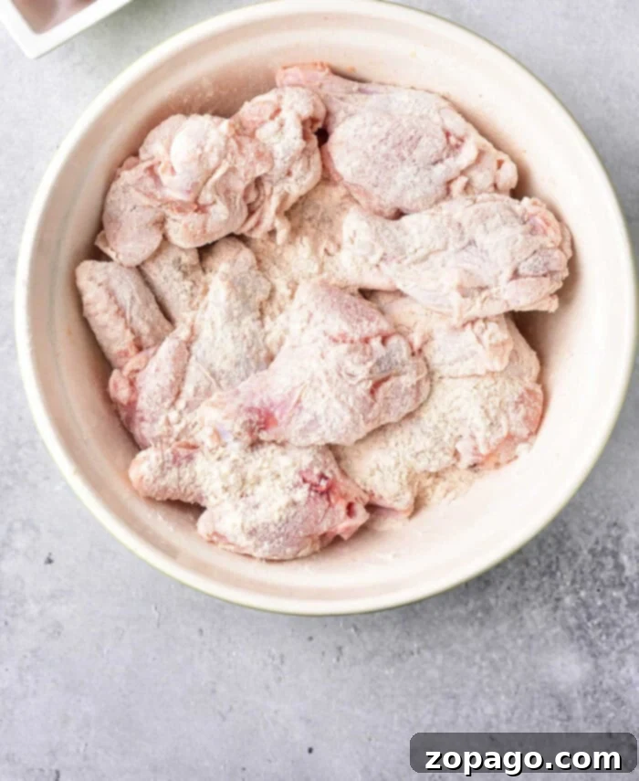 Unlock Crispy Baked Wings at 425 3 Raw chicken wings evenly coated with baking powder in a white bowl, ready for baking.